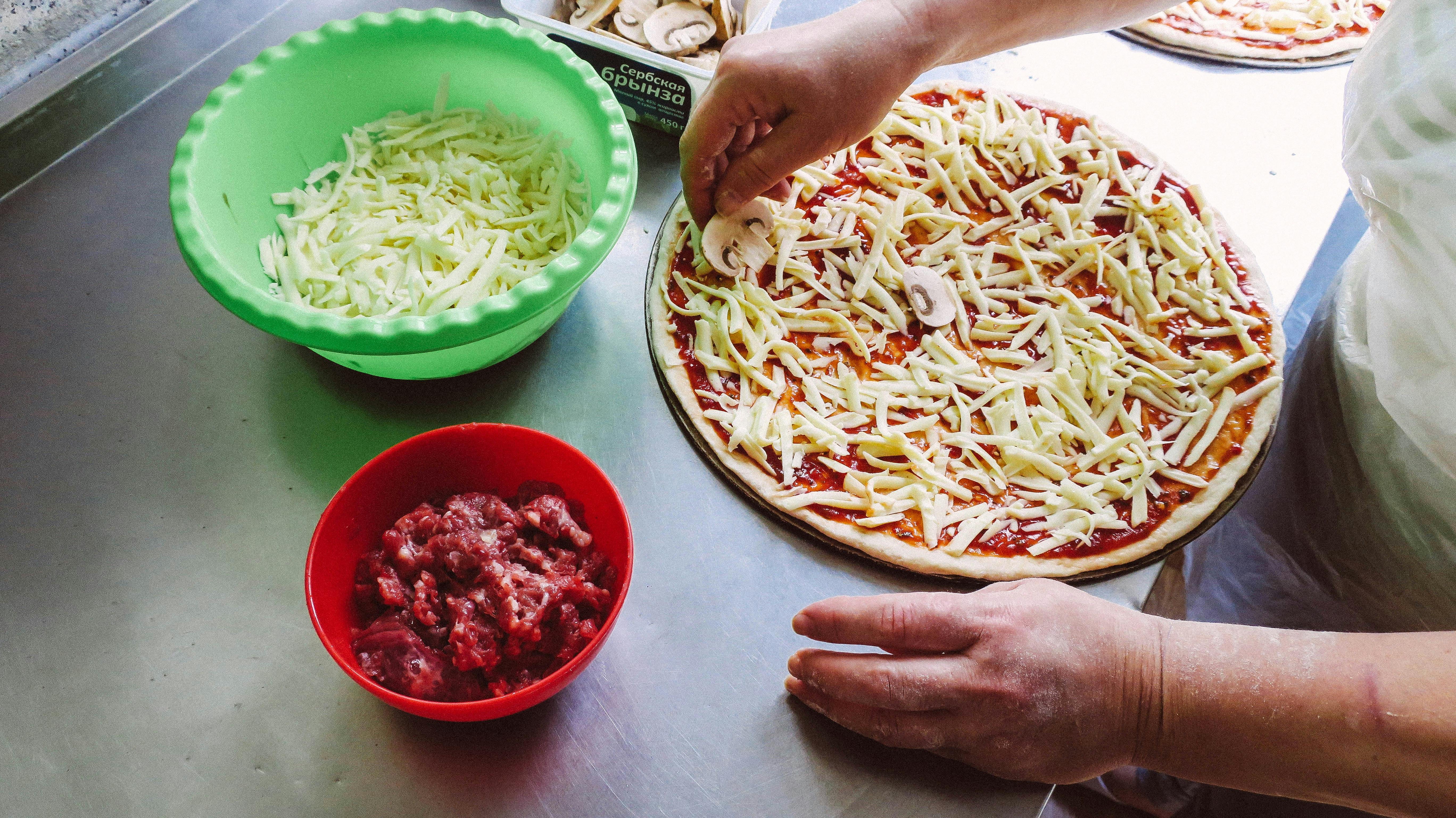 Person preparing pizza with cheese and tomato sauce