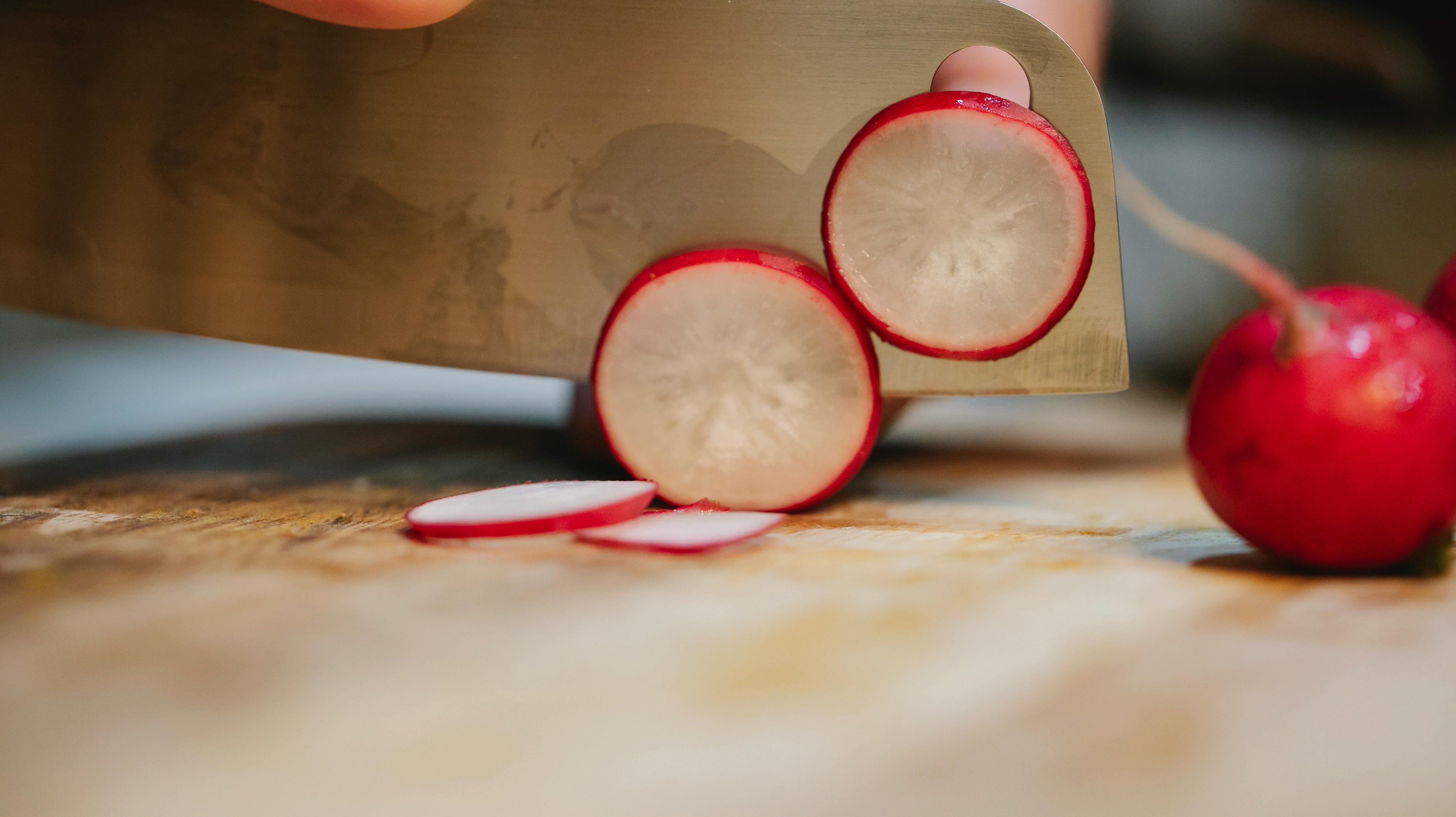 A large knife thinly slicing red radishes