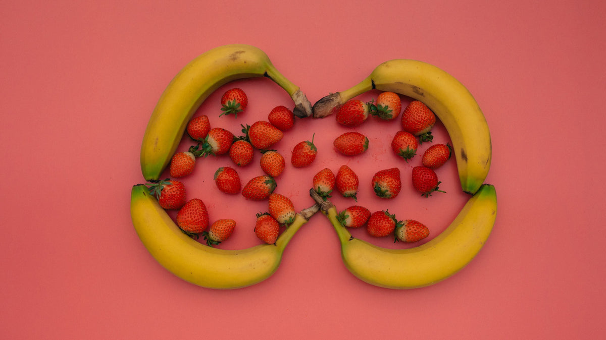 Bananas circling a small group of strawberries on a pink background