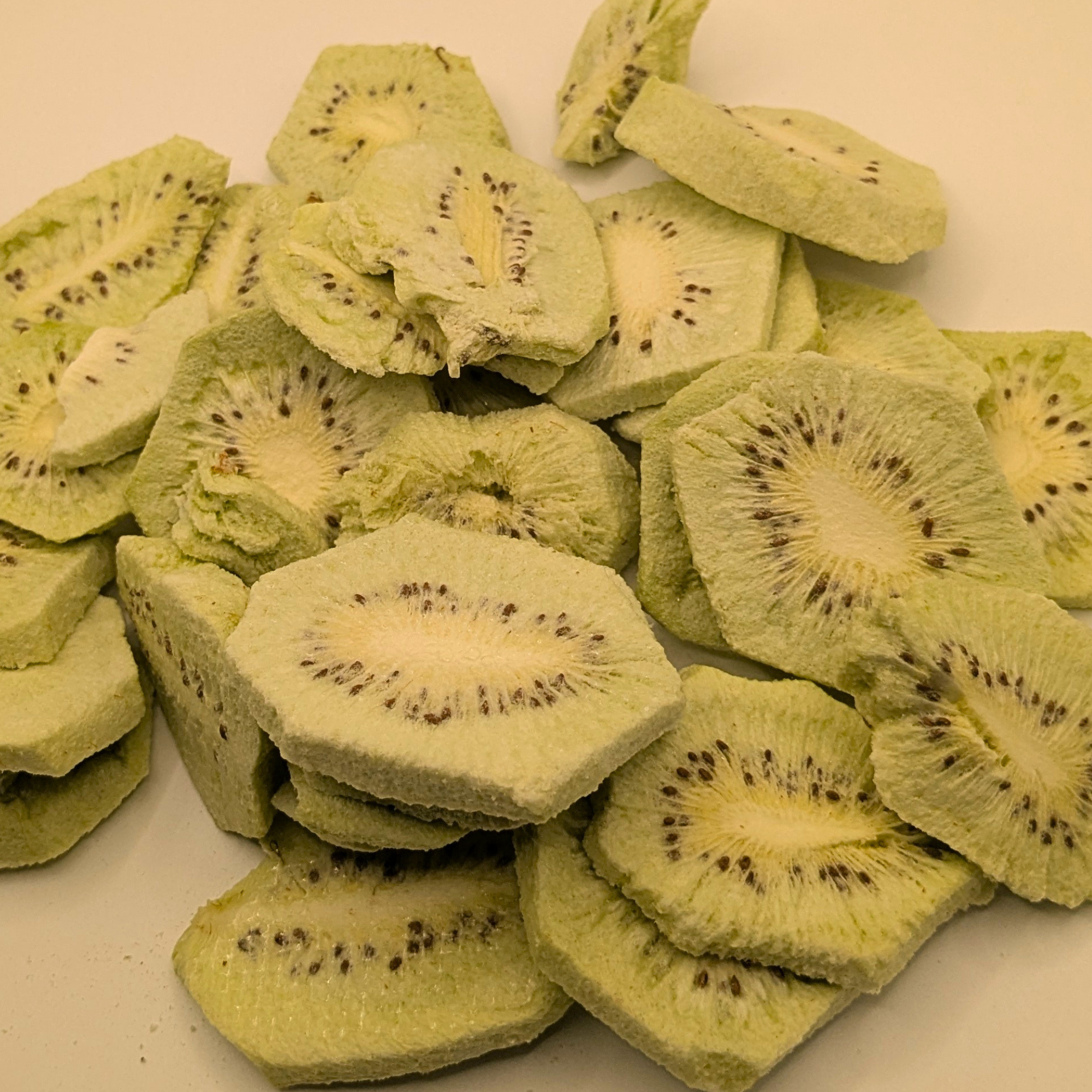A pile of slice freeze dried kiwis on a white surface