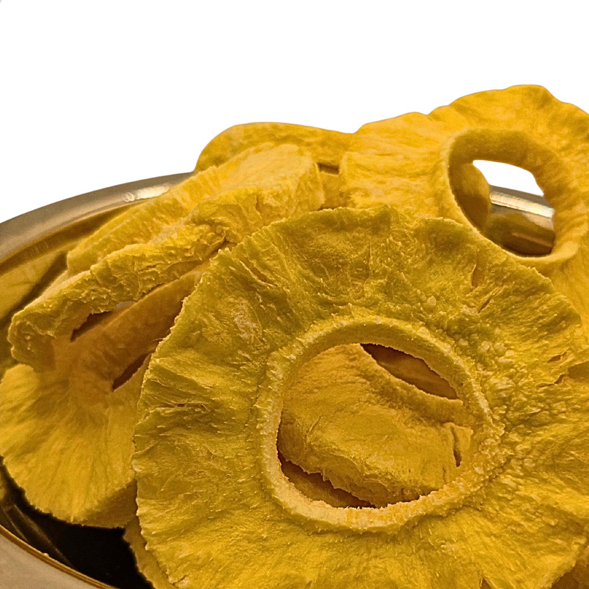 Yellow freeze dried pineapple slices stacked in a silver bowl against a white background.