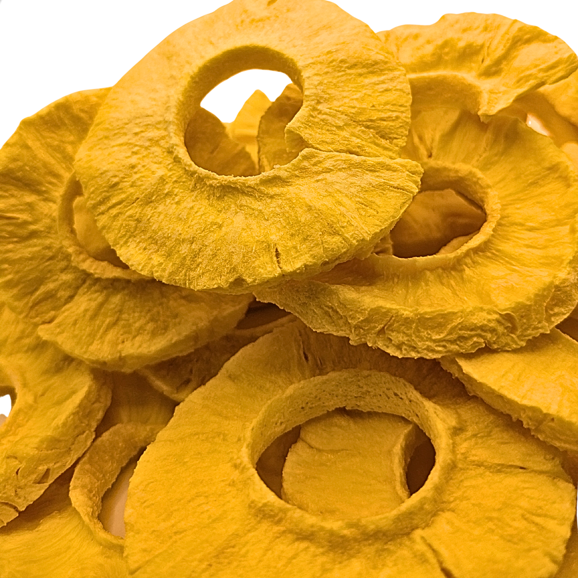 A close-up pile of freeze dried pineapple slices with a bright yellow-orange hue, showing their textured, fibrous structure against a white background.