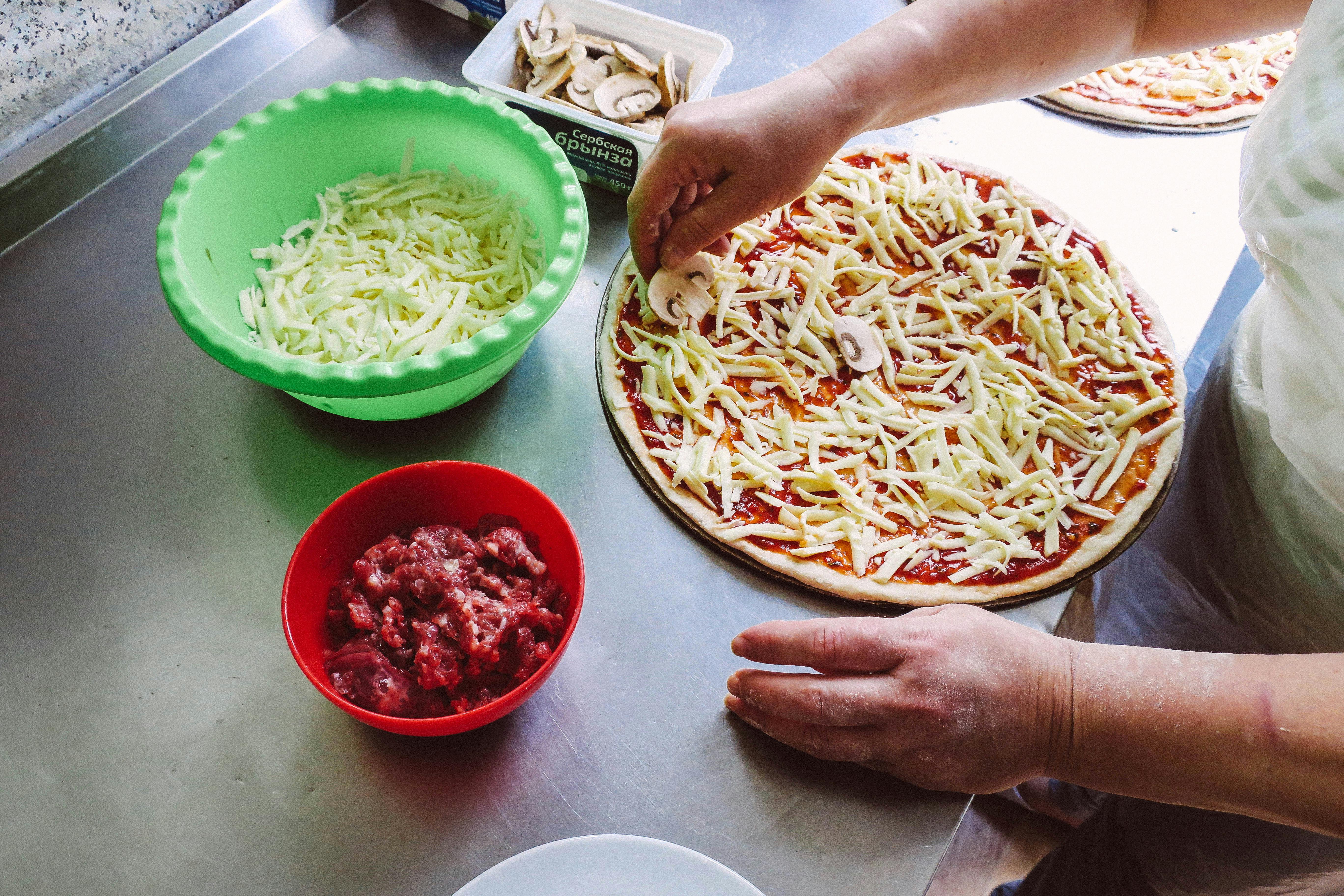 Person preparing pizza with cheese and tomato sauce