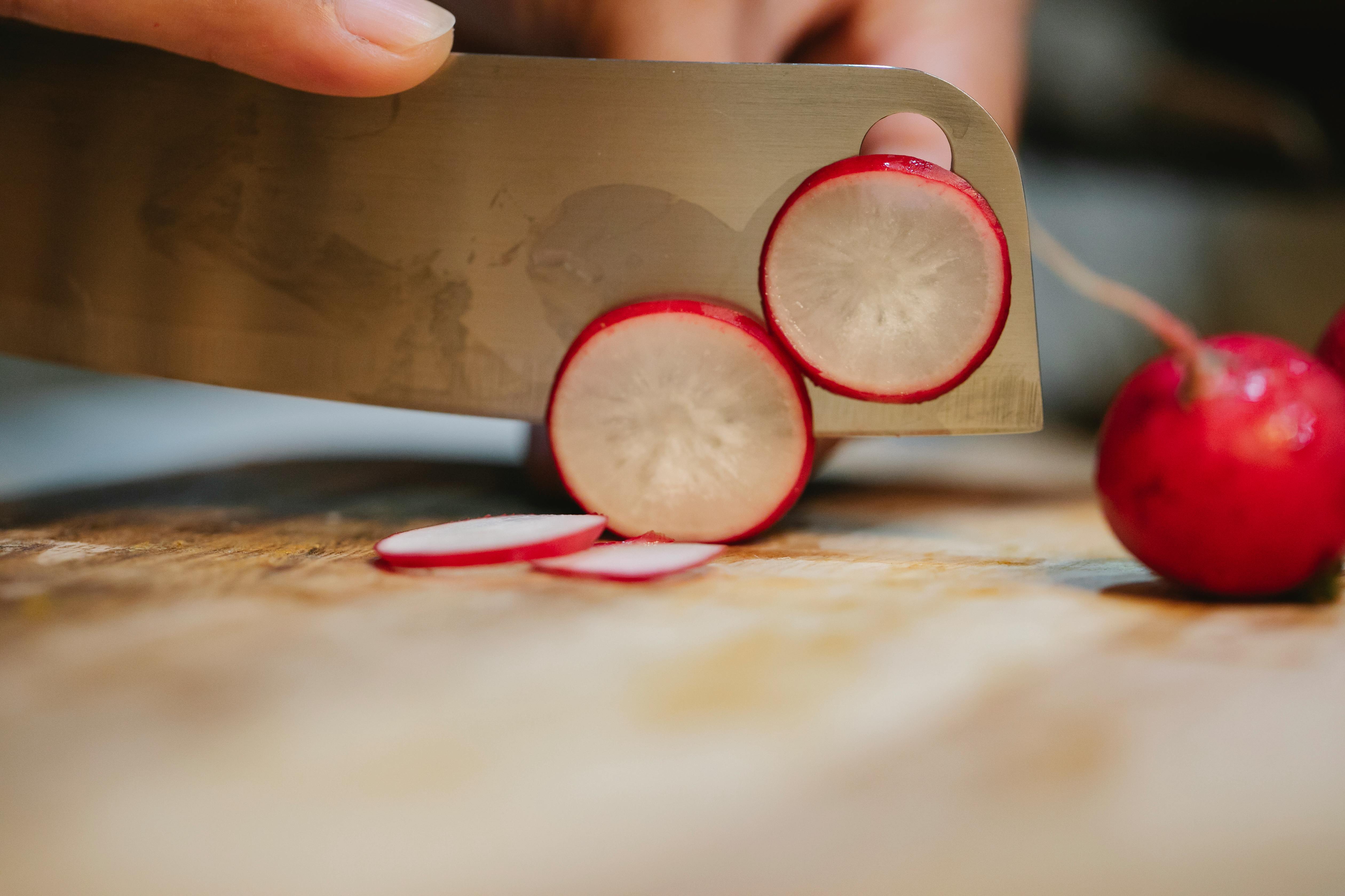 A large knife thinly slicing red radishes