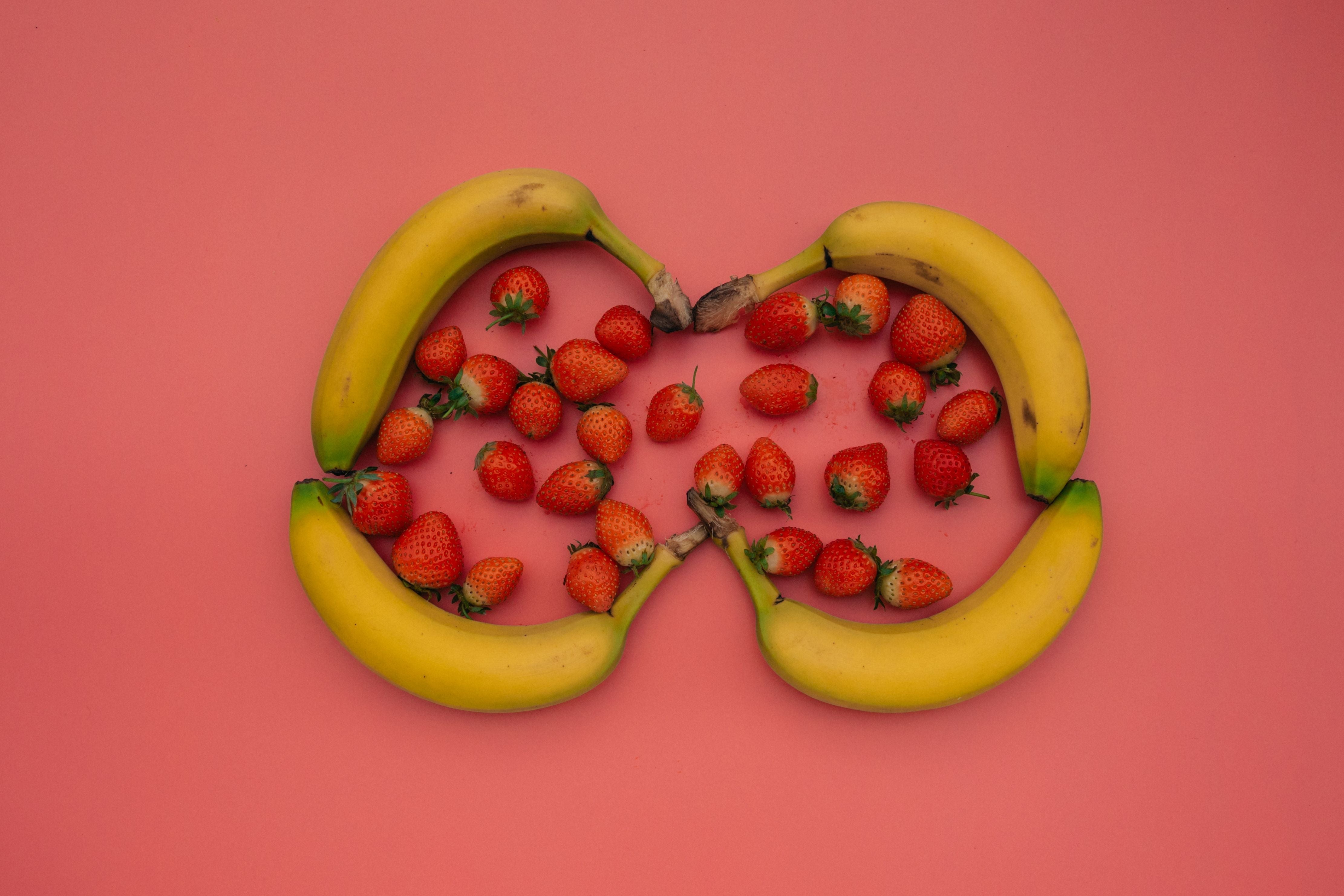 Bananas circling a small group of strawberries on a pink background