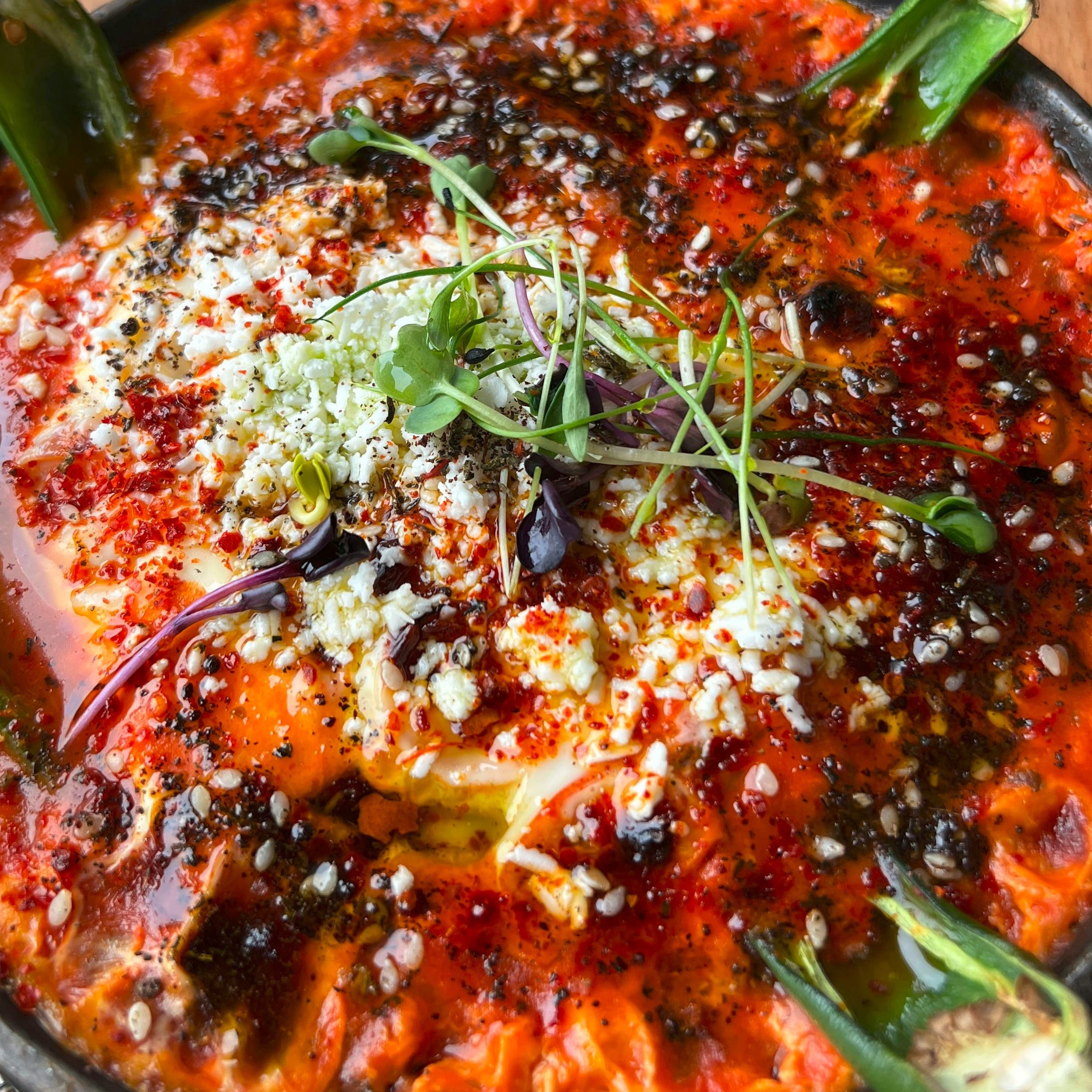 A red cheese dish with green peppers topped with green microgreens