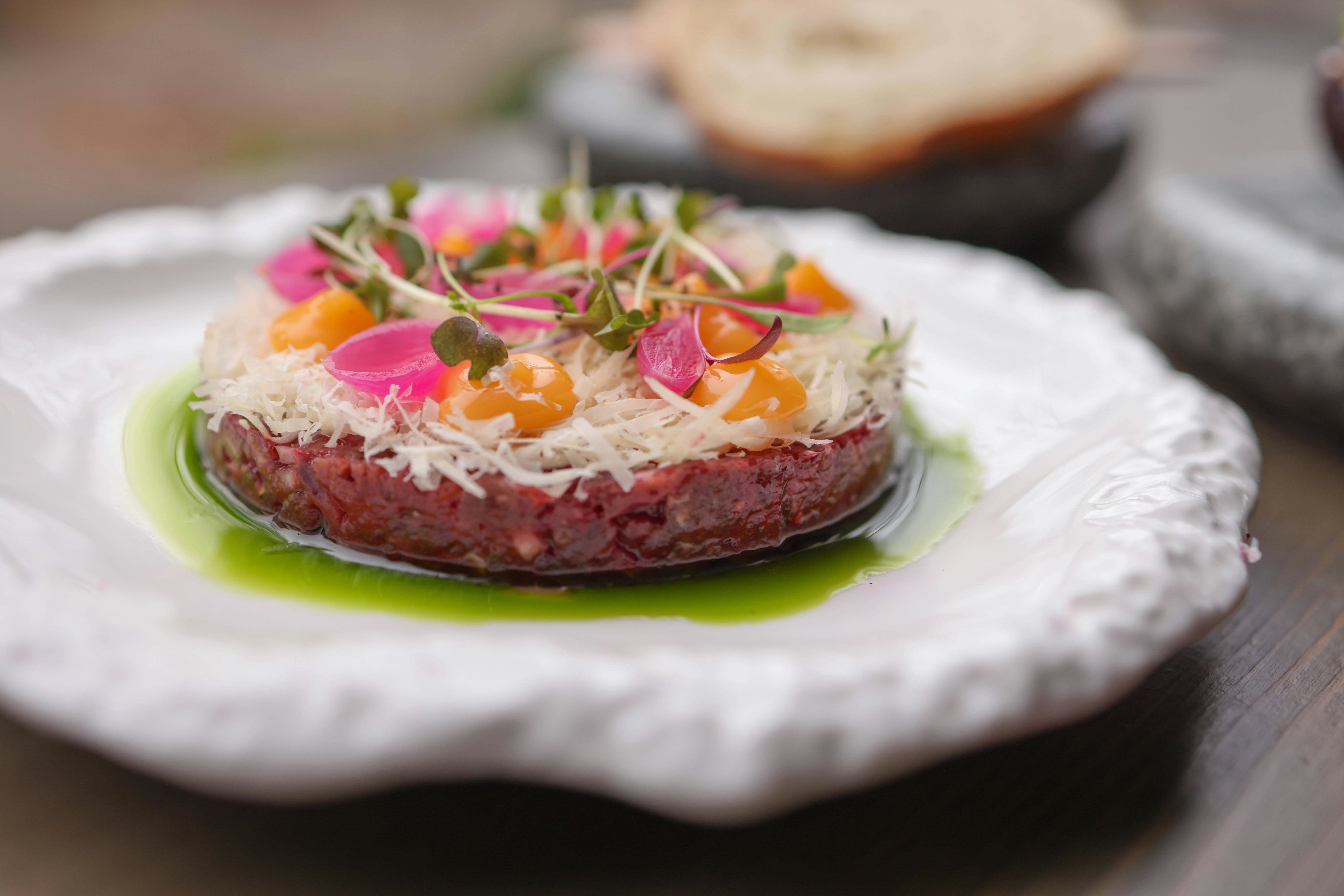 Beef tartare topped with beetroot and microgreens on a white plate 
