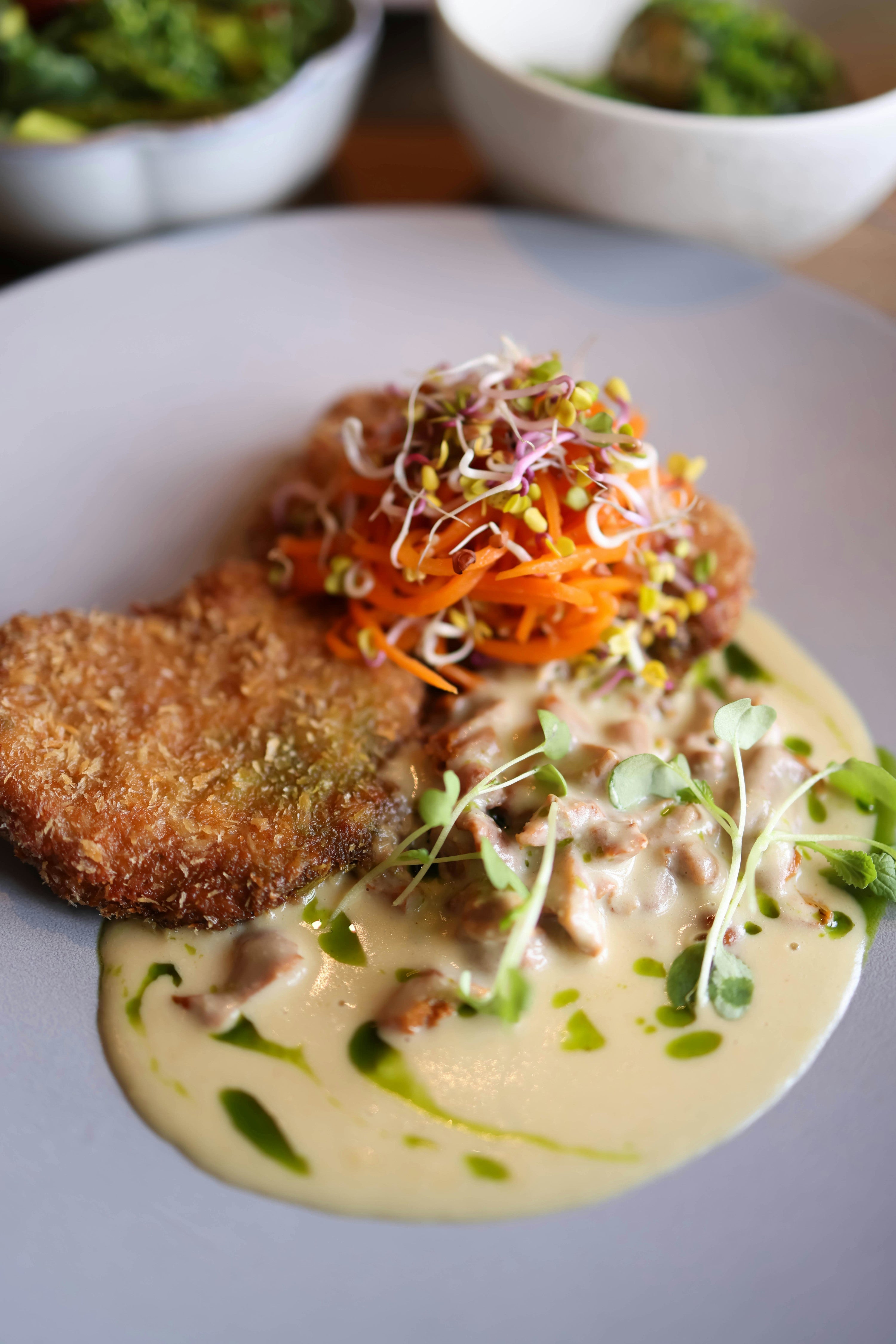 Broccoli microgreens topping a chicken cutlet with shredded carrots and a creamy sauce