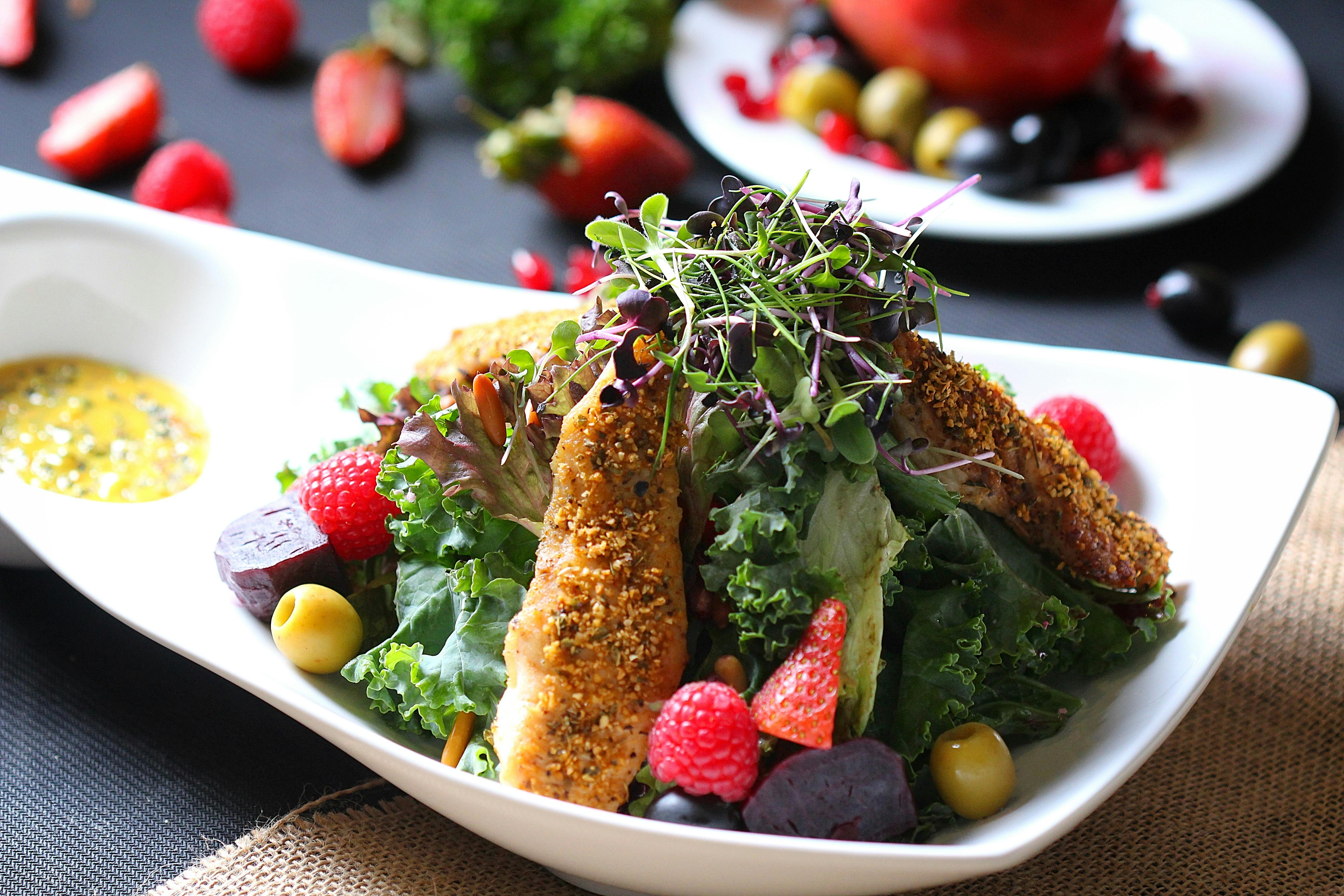 Grilled chicken, kale, and fruit topped with microgreens on a white plate with dressing on the side