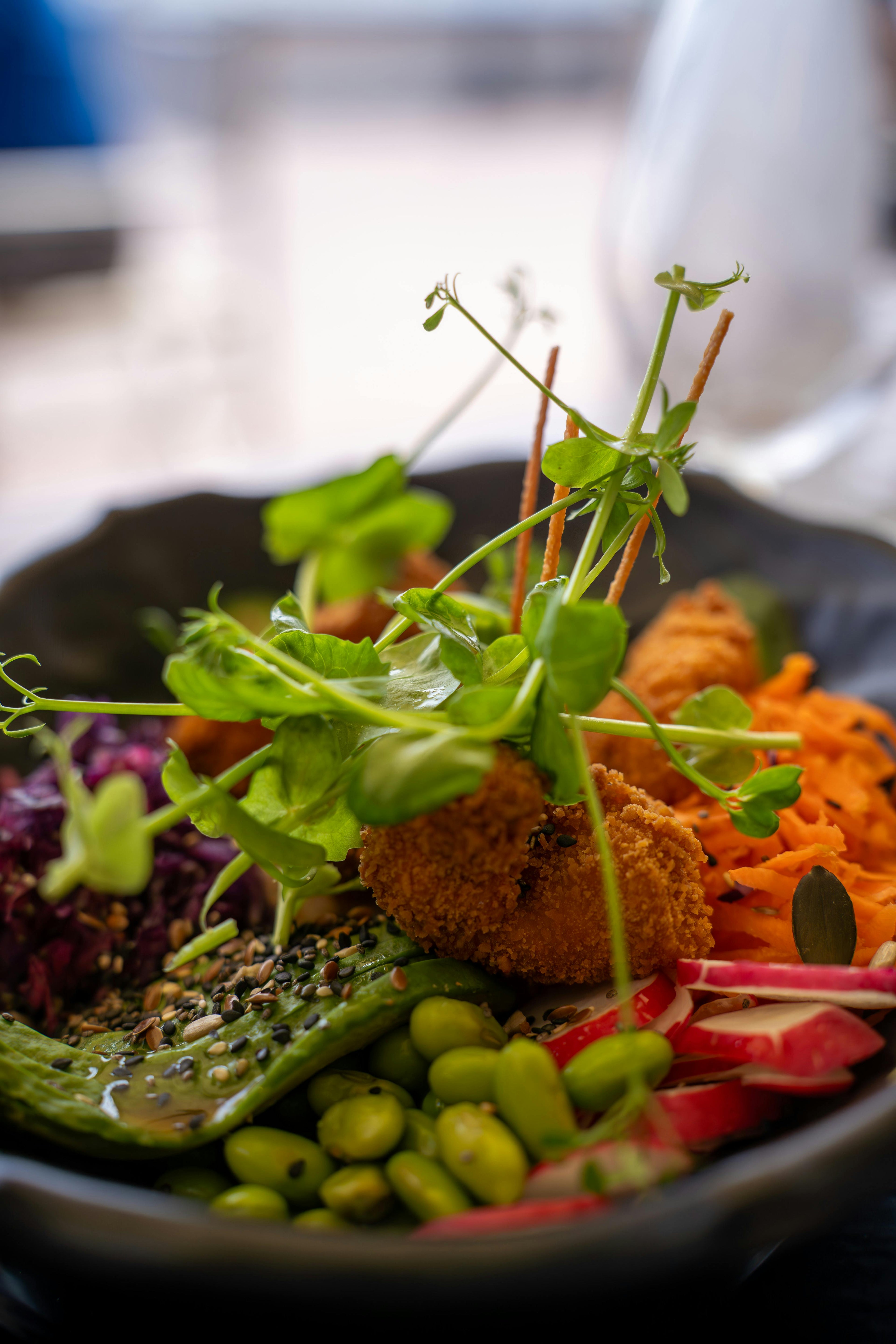 Microgreens topping a bowl with carrots, edamame beans, and radish.