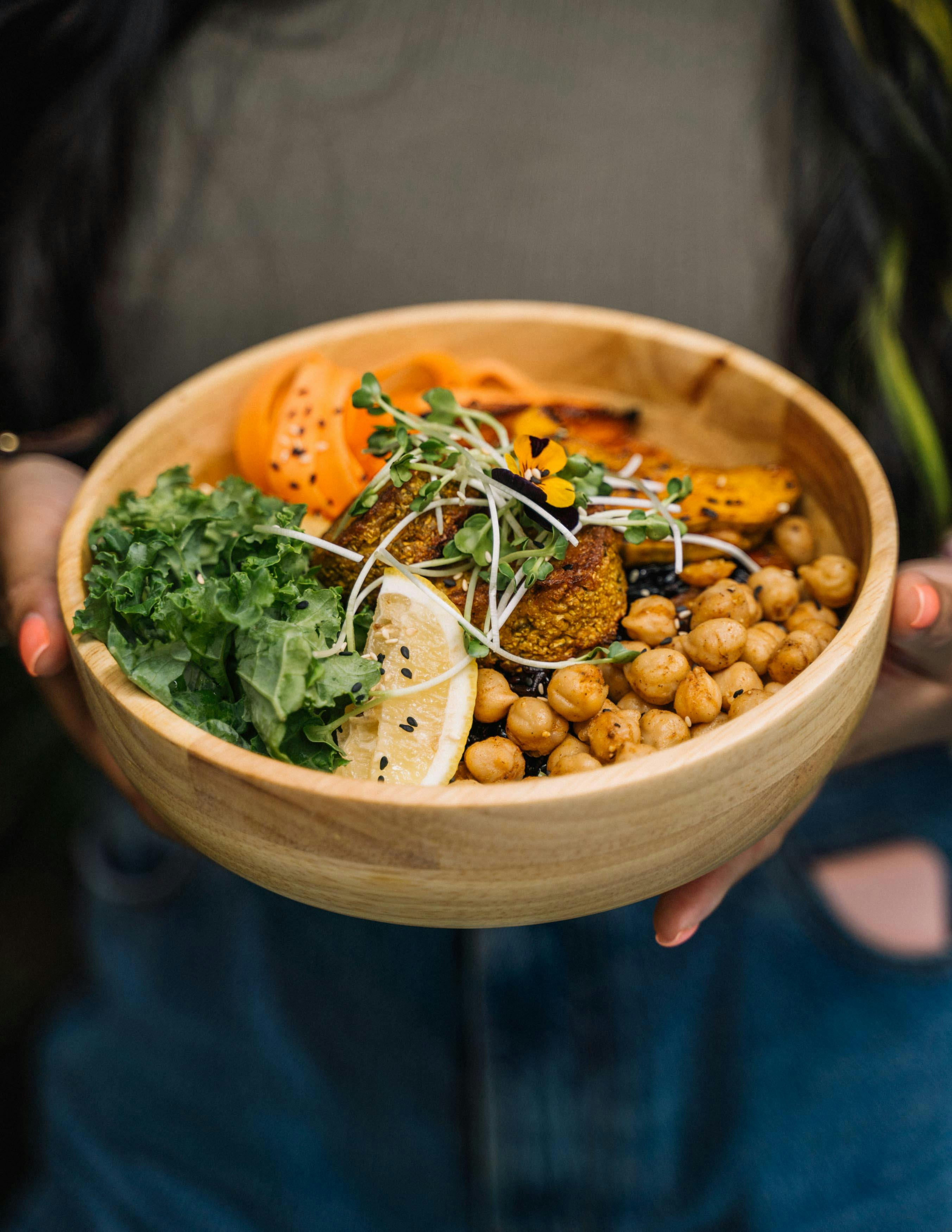 A person holding a bowl with chickpeas, lemon, and kale topped with microgreens