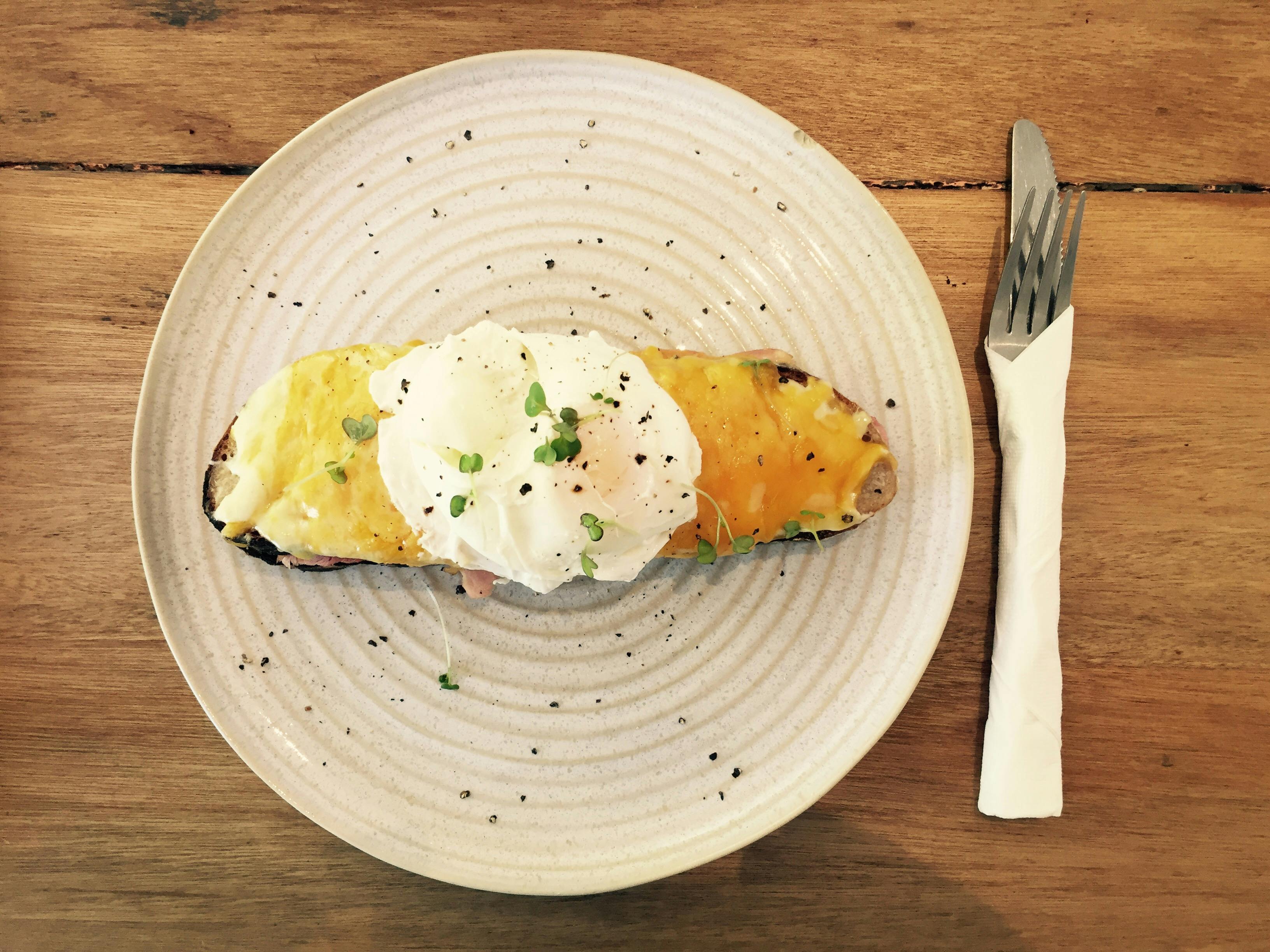 Eggs bennedict topped with microgreens on cheese-covered toast on a plate with a fork and knife wrapped in a napkin