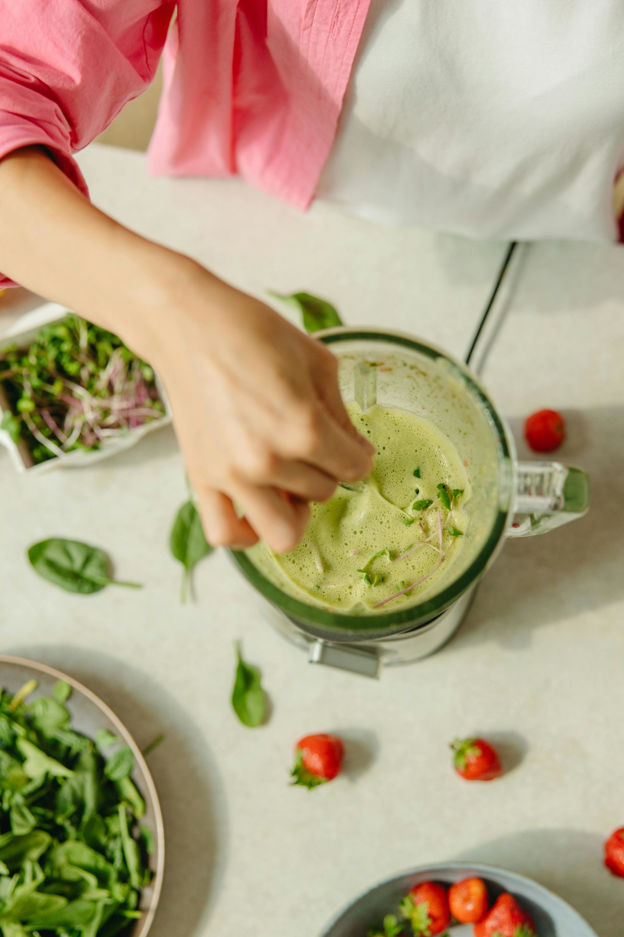 A green smoothie being prepared in a blender with microgreens and strawberries