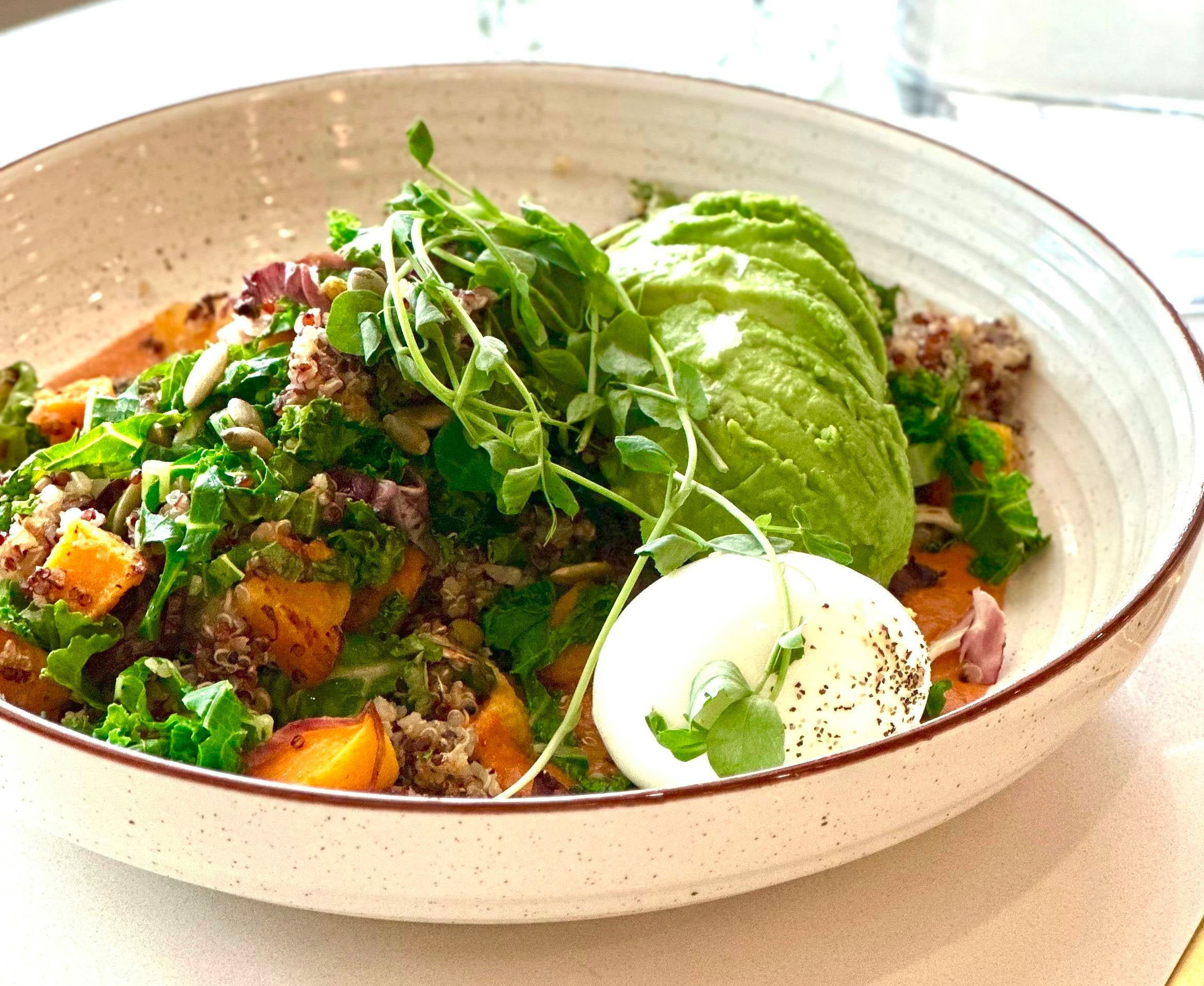 A bowl with avocado, eggs, and microgreens on a table
