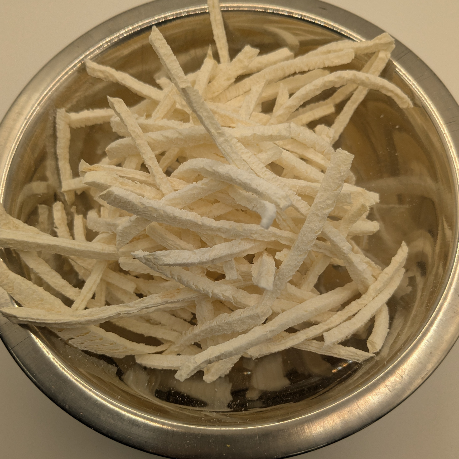 Freeze dried jicama in a metal bowl on a white background