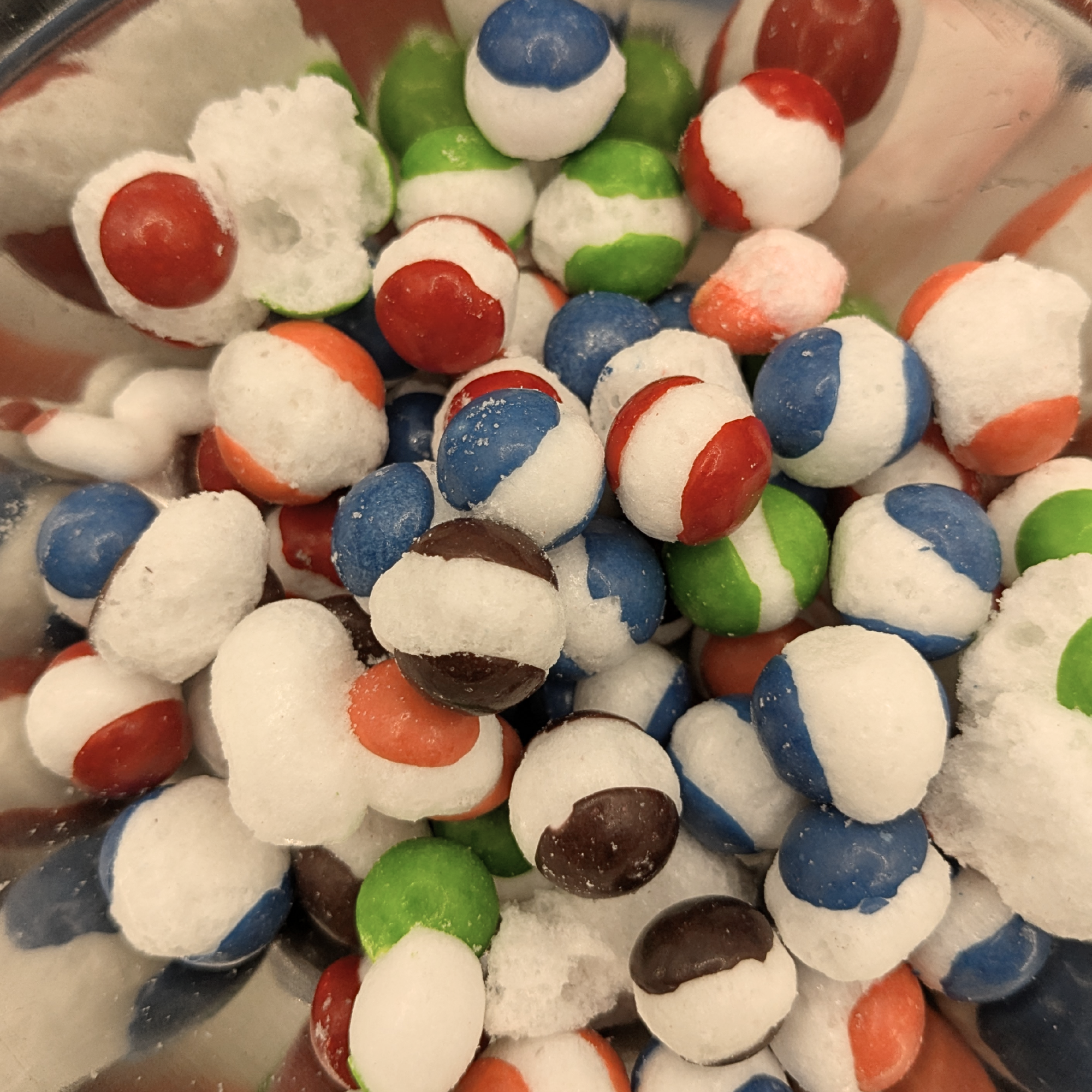 A close-up of a bowl filled with small candy showing red, blue, green, orange, and brown candy colors mixed with white sugar.