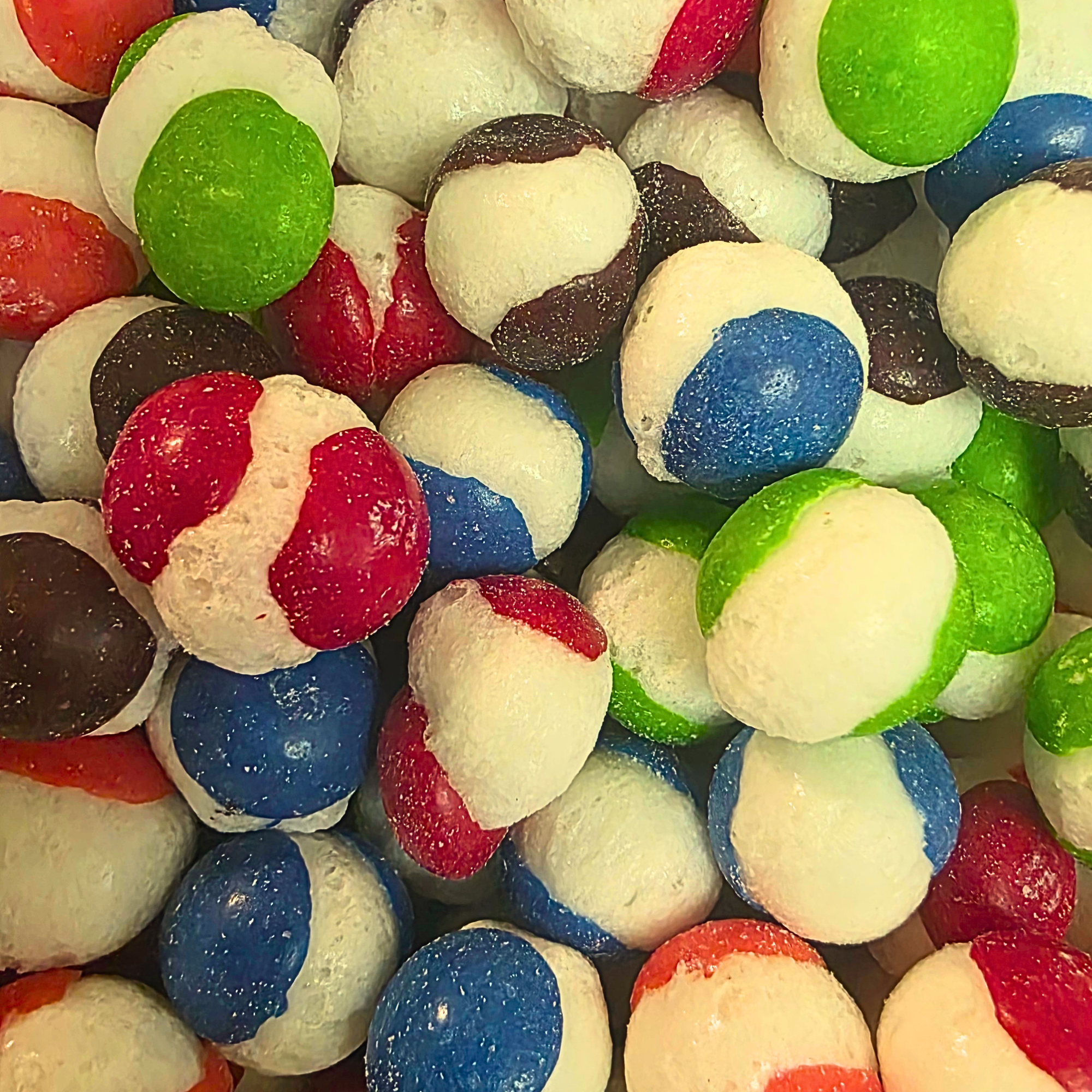Freeze dried candy, which is white in the center like its burst with a colorful outer shell in red, green, pink, and black, that resemble freeze dried skittles
