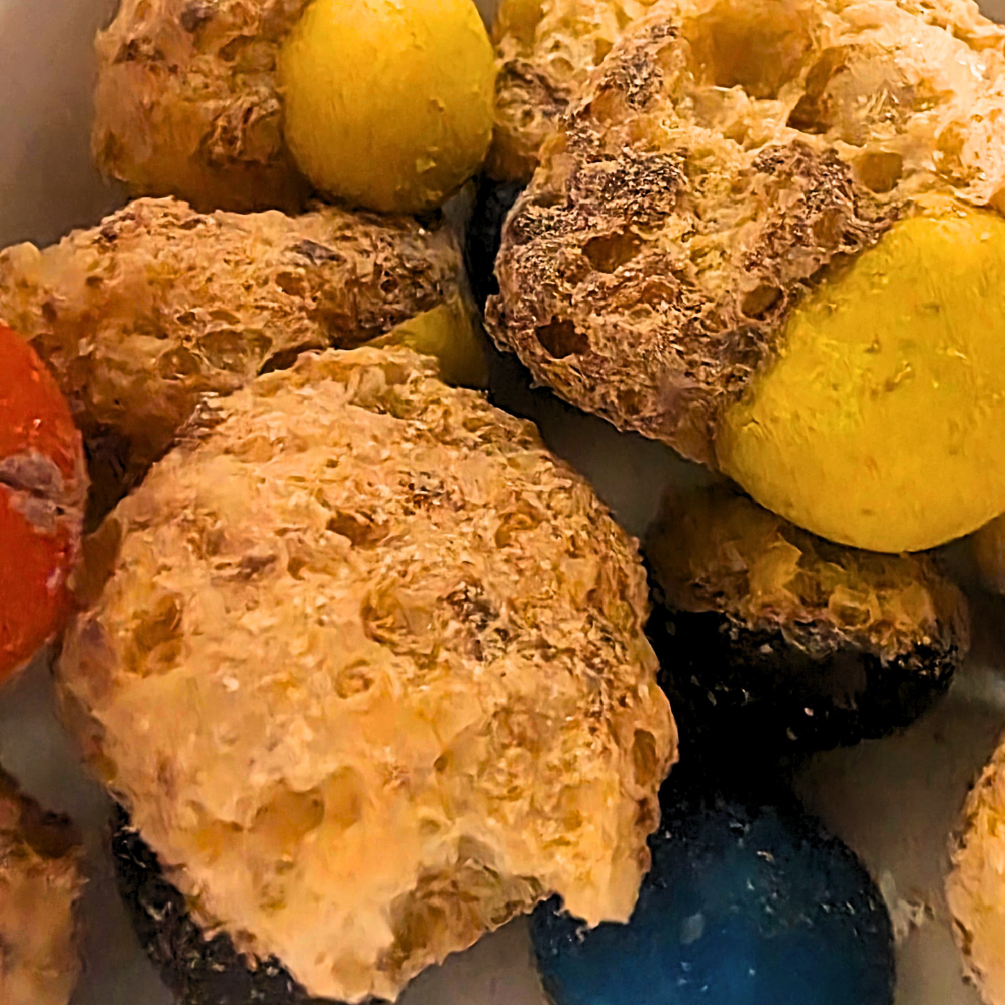Freeze dried caramel and chocolate candy, where the center has burst and the outer candy shells are visible in orange, yellow, blue, and dark purple