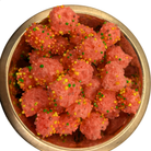 A top-down view of pink, crispy freeze dried candy coated with colorful sprinkles, served in a round metallic bowl against a white background.