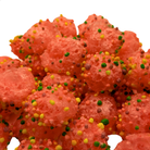 A close-up pile of bright pinkish-red candy covered with small multicolored sprinkles, photographed against a plain white background.