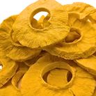A close-up pile of freeze dried pineapple slices with a bright yellow-orange hue, showing their textured, fibrous structure against a white background.