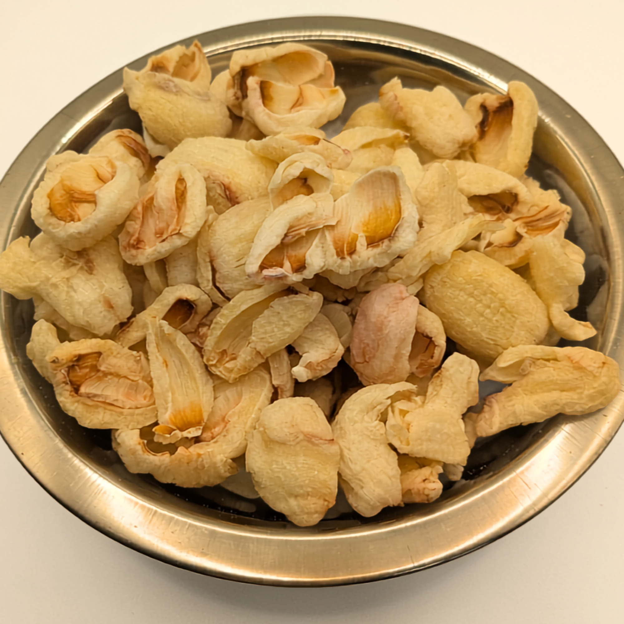 A metal bowl of freeze dried lychee berries on a white background